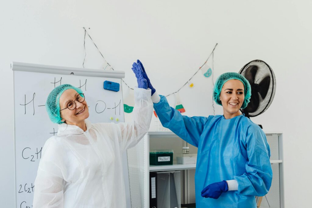 Two healthcare professionals in PPE high-fiving in a lab, exuding positivity after medical waste training.